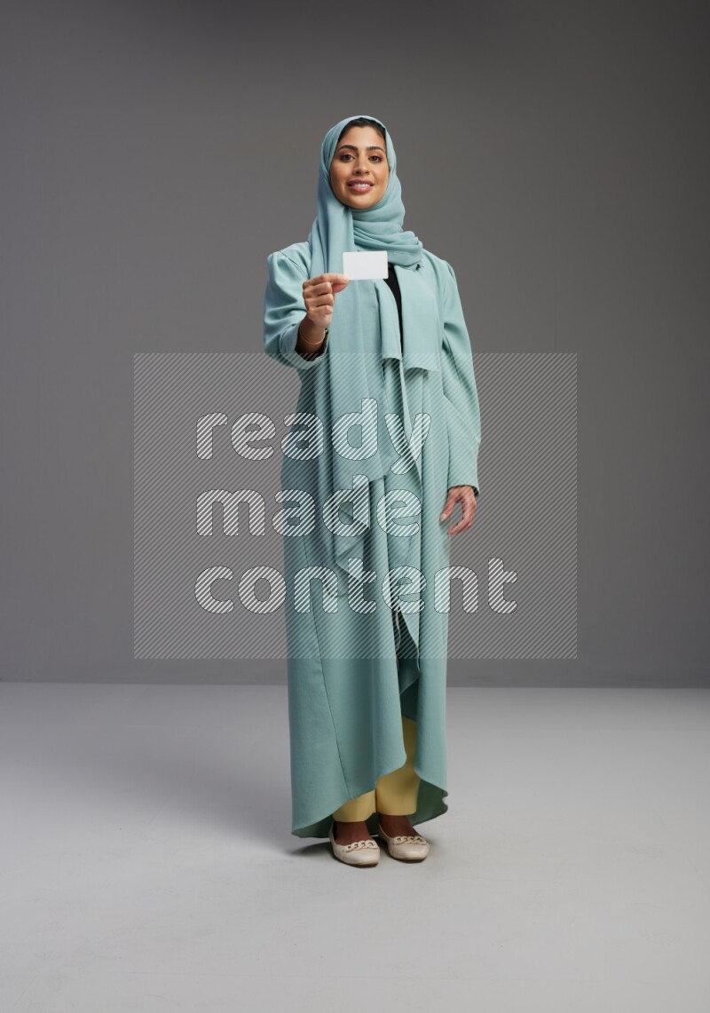 Saudi Woman wearing Abaya standing holding ATM card on Gray background