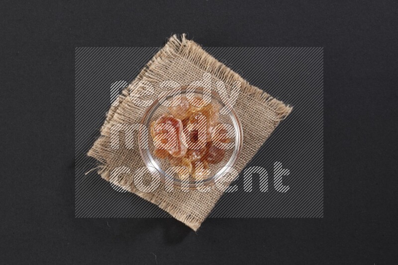 A glass bowl full of gum arabic on a burlap piece on black flooring