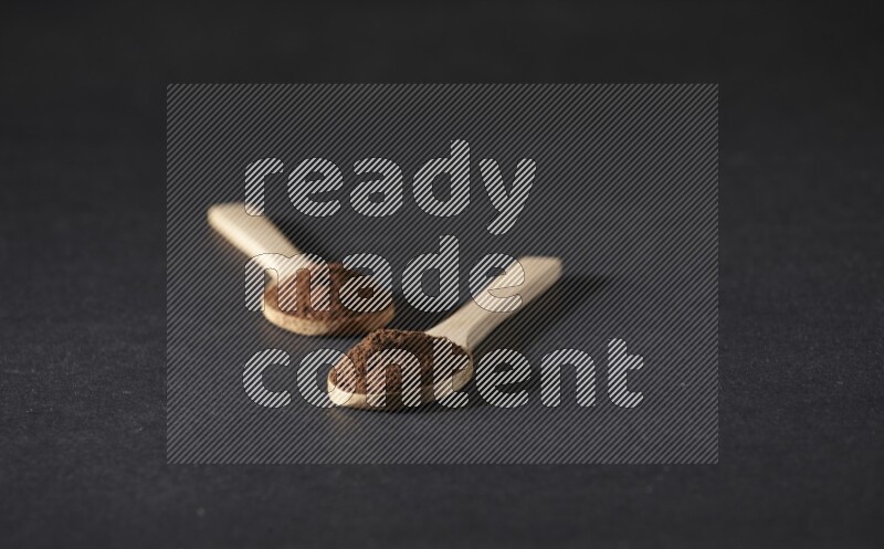 ملعقتان خشبيتان ممتلئتان ببودرة القرنفل على خلفية سوداء