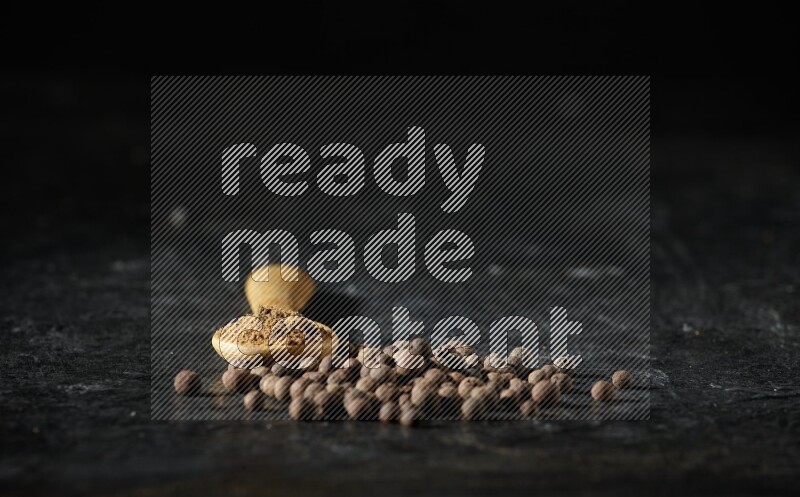 ملعقة خشبية ممتلئة ببودرة بهار الفلفل الحلو بجانب حبوب من الفلفل على خلفية سوداء