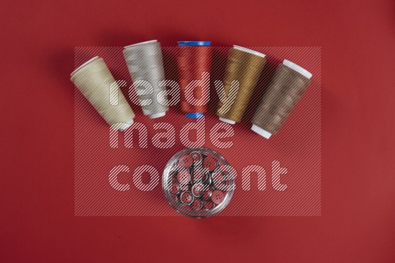 A brown and red collection of sewing and tailoring tools arranged on a red background