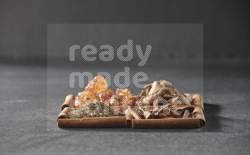 4 مربعات من عيدان القرفة ممتلئة بالصمغ العربي والزنجبيل المجفف وقطع القرفة والكمون على أرضية سوداء