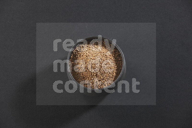 A black pottery bowl full of mustard seeds on black flooring