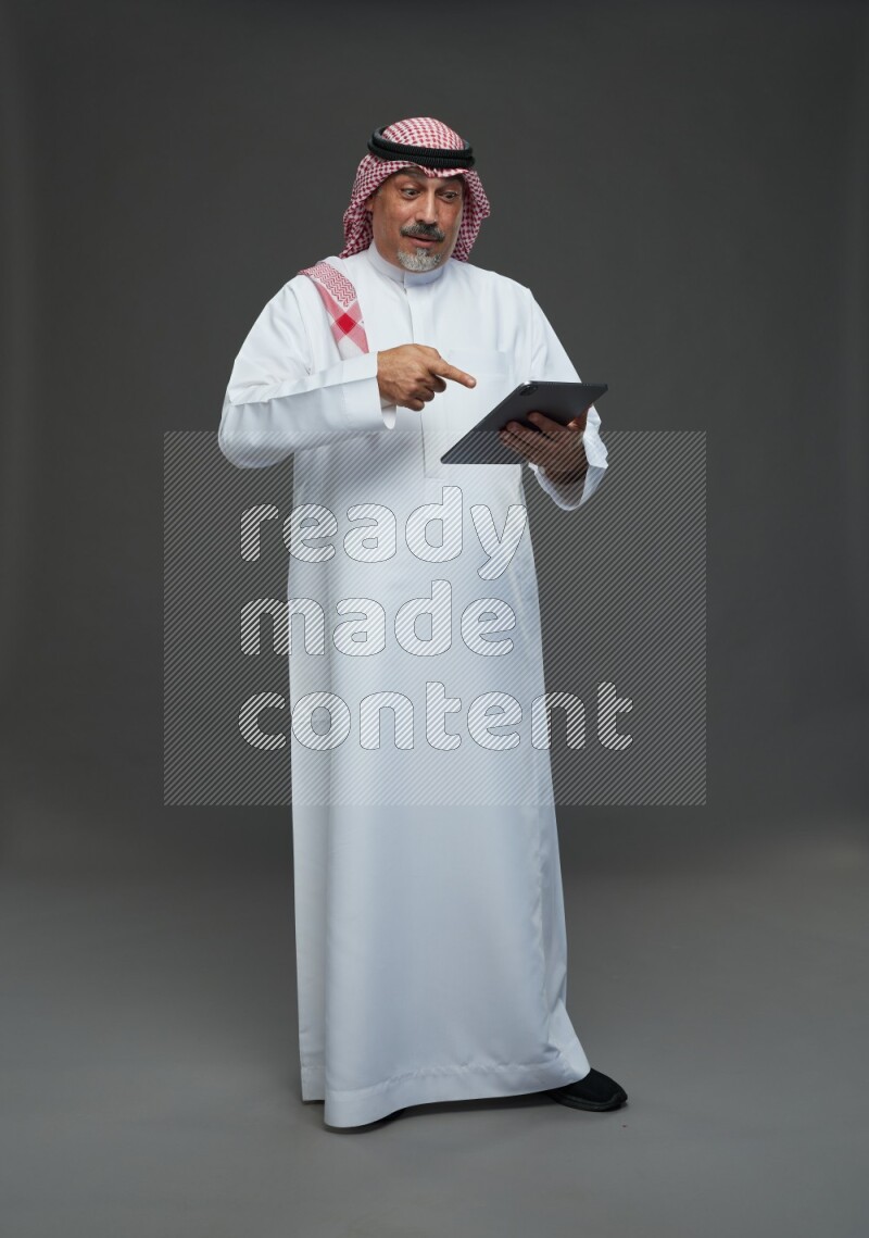 Saudi man with shomag Standing working on tablet on gray background