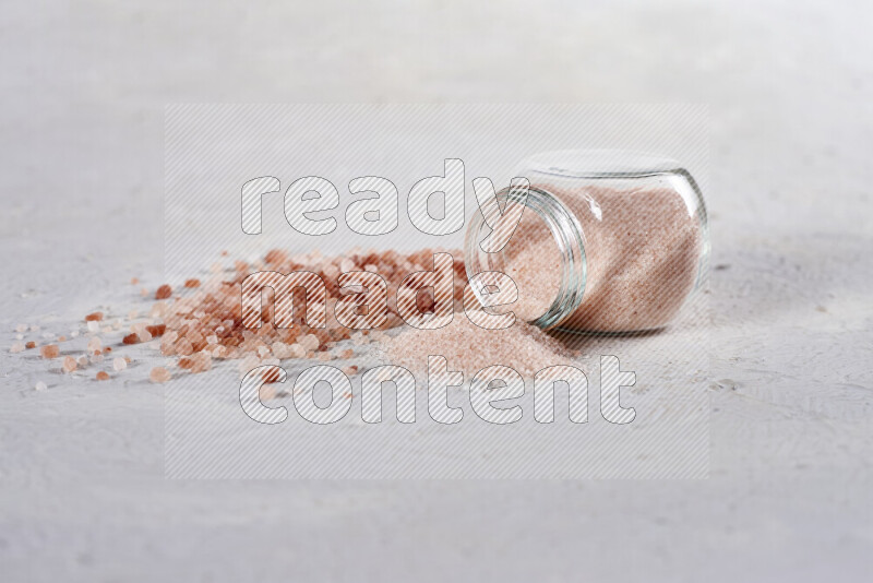 A glass jar full of fine himalayan salt with some himalayan crystals beside it on a white background