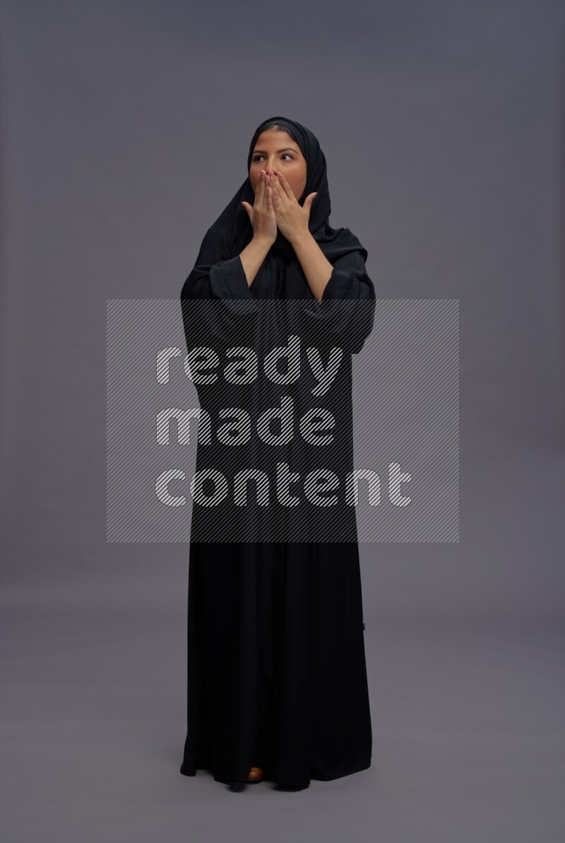 Saudi woman wearing Abaya standing hands behind head on gray background