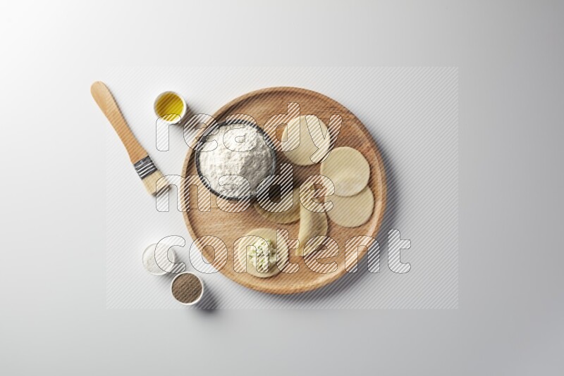 two closed sambosas and one open sambosa filled with cheese while flour, salt, black pepper and oil with oil brush aside in a wooden dish on a white background
