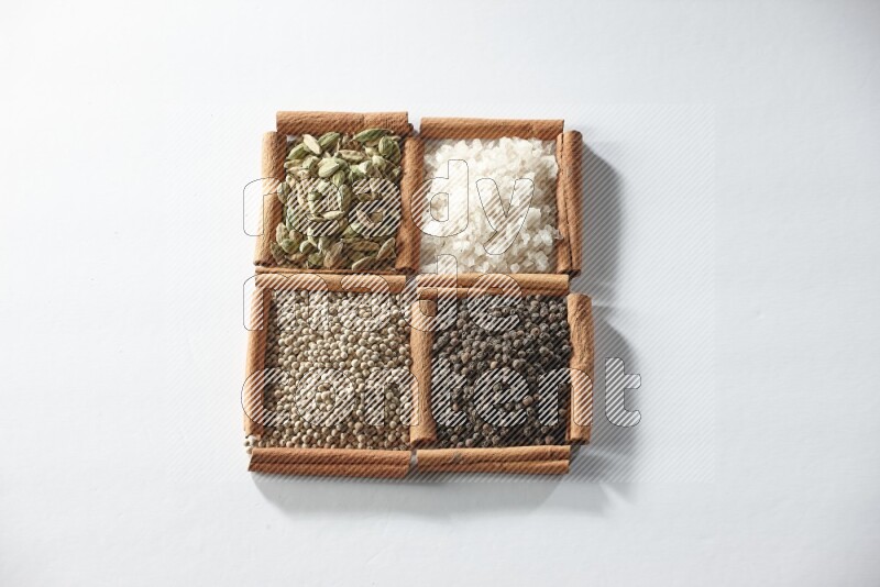 4 مربعات من أعواد القرفة ممتلئة بالهيل والملح والفلفل الأبيض والفلفل الأسود على أرضية بيضاء