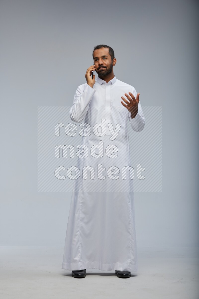 Saudi man wearing Thob standing talking on phone on Gray background