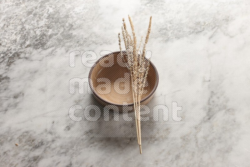 Wheat stalks on beige pottery oven bowl on grey marble background