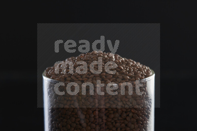 Brown lentils in a glass jar on black background