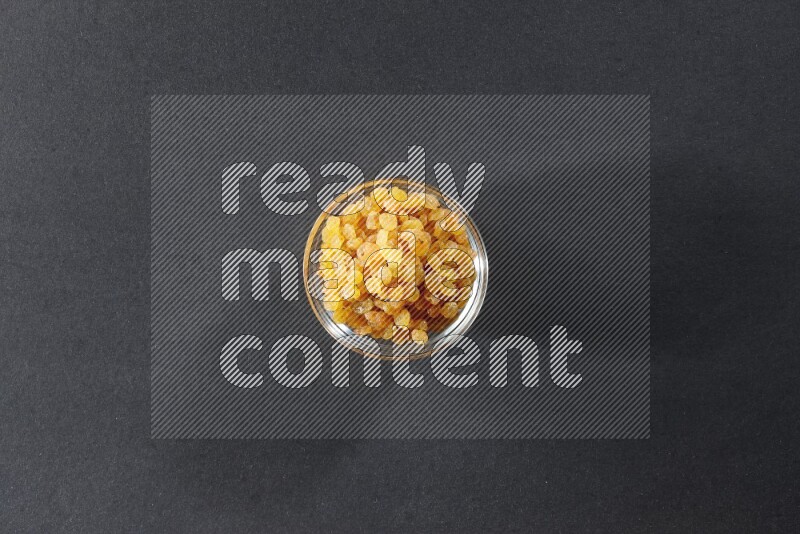 A glass bowl full of raisins on a black background in different angles