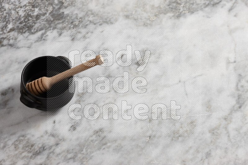 وعاء فخاري أسود مع ملعقة عسل خشبية بداخله على خلفية من الرخام الرمادي
