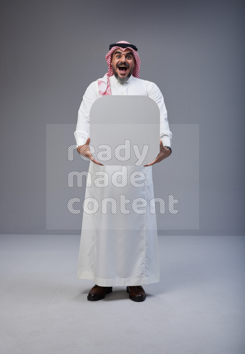 Saudi man Wearing Thob and red Shomag standing holding social media sign on Gray background