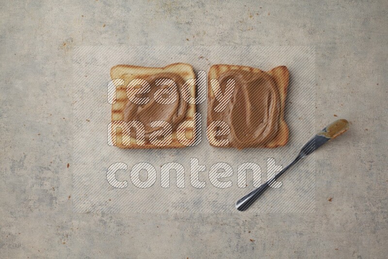 Creamy peanut butter on a toasted white toast slices with a spreading knife on a light blue textured background