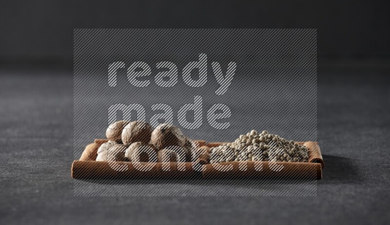 2 squares of cinnamon sticks full of nutmeg and white peppers on black flooring