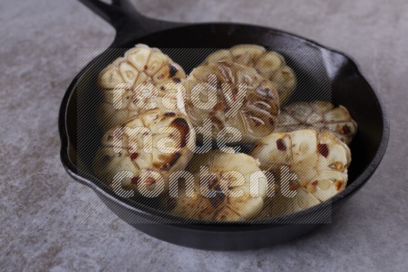half's roasted garlic in a black pan on a grey textured countertop