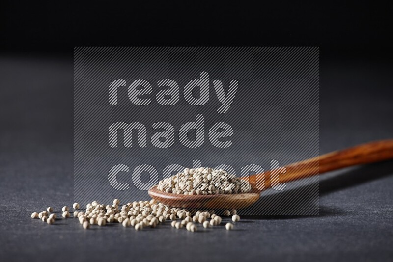 A wooden ladle full of white pepper beads on black flooring