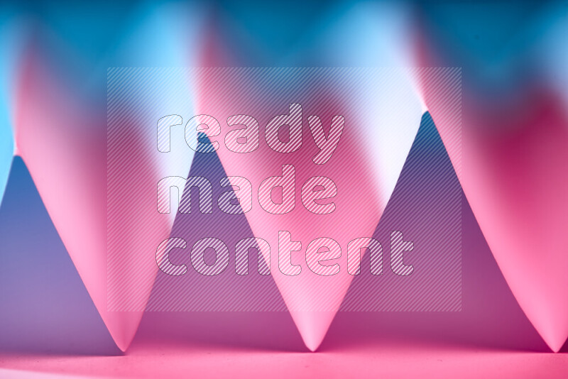 A close-up abstract image showing sharp geometric paper folds in blue and pink gradients