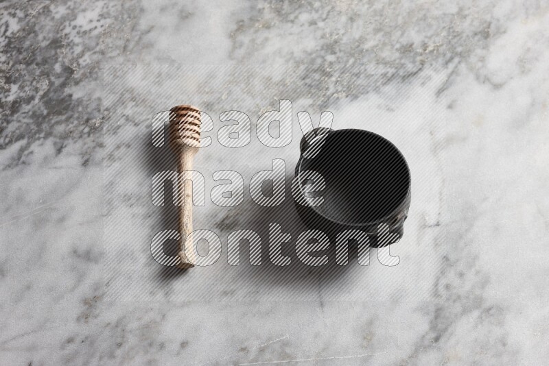 Black pottery bowl with wooden honey dipper on the side on grey marble background