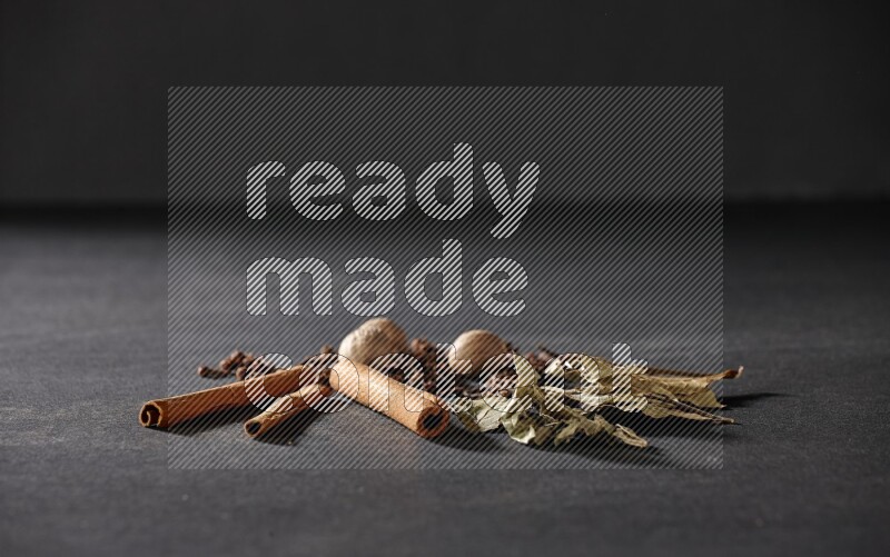 Cloves, ginger, bay laurel and cinnamon sticks on black flooring
