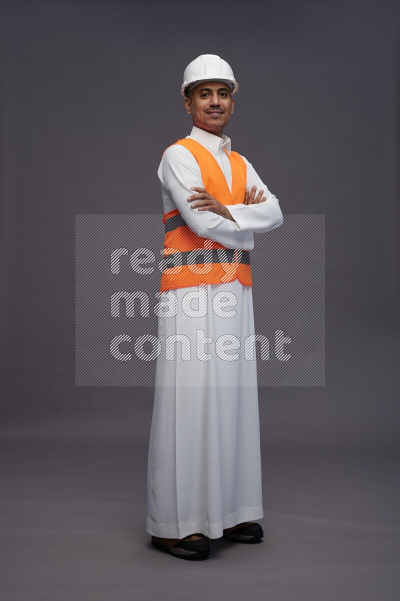 Saudi man wearing thob with engineer vest standing with crossed arms on gray background