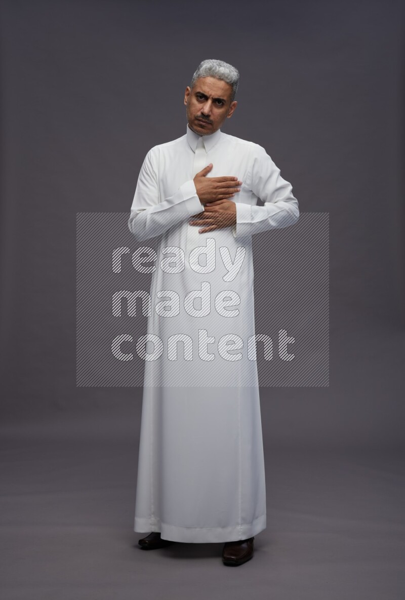 Saudi man wearing thob standing interacting with the camera on gray background