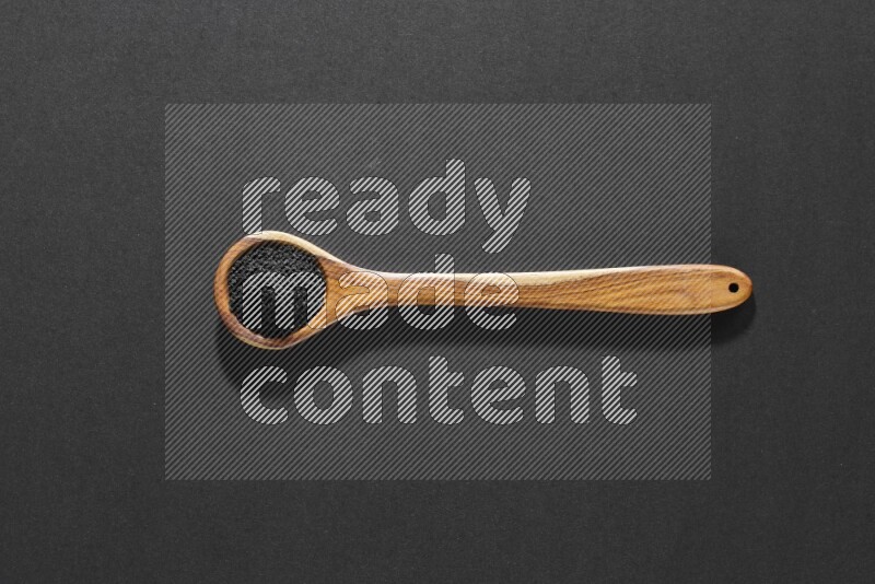 A wooden ladle full of black seeds on a black flooring