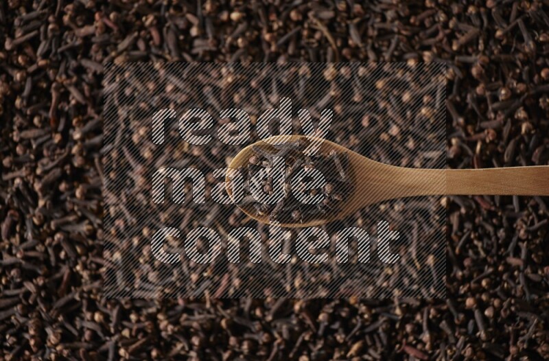A wooden spoon full of cloves on cloves background and black flooring