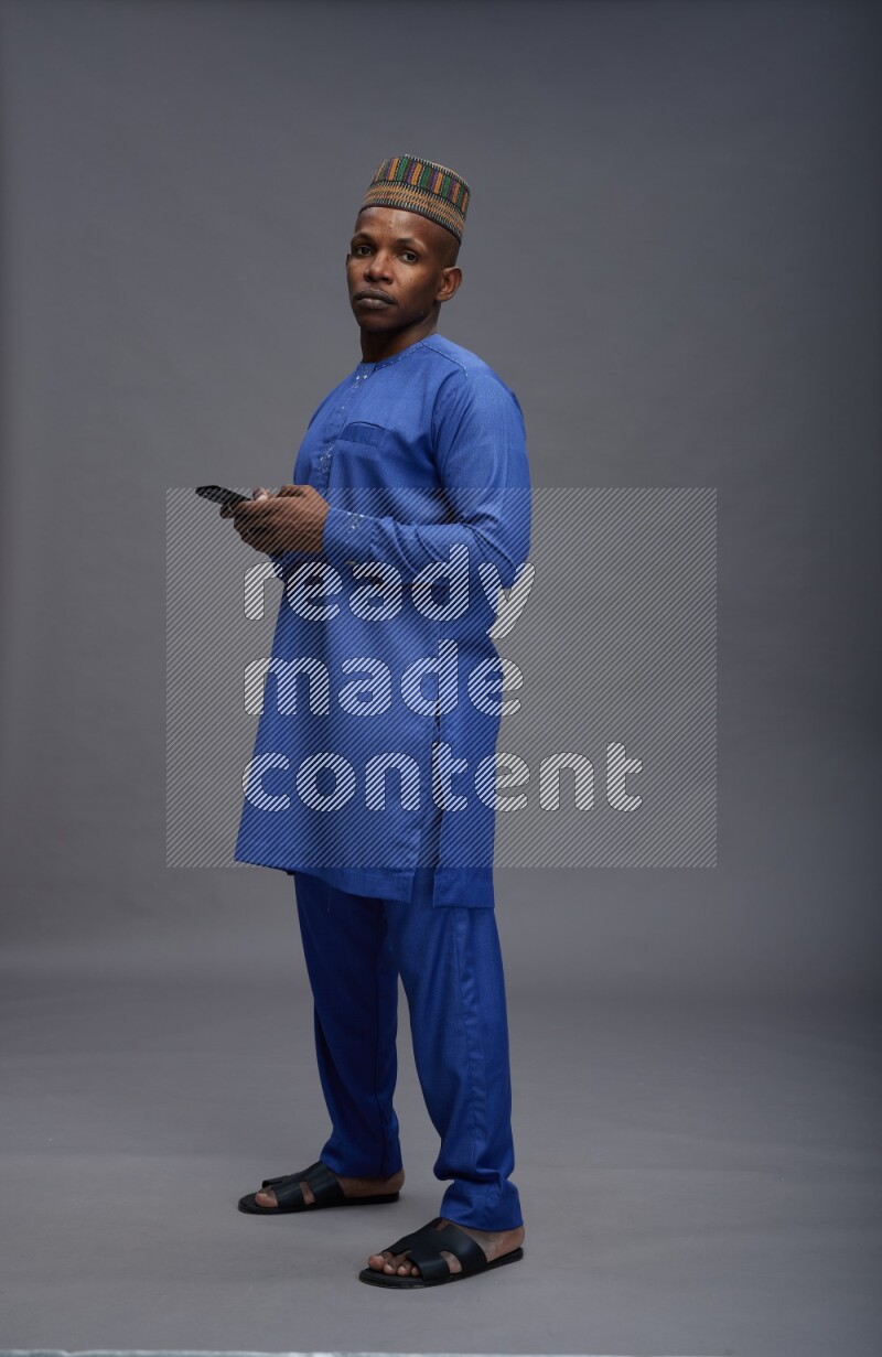 Man wearing Nigerian outfit standing texting on phone on gray background
