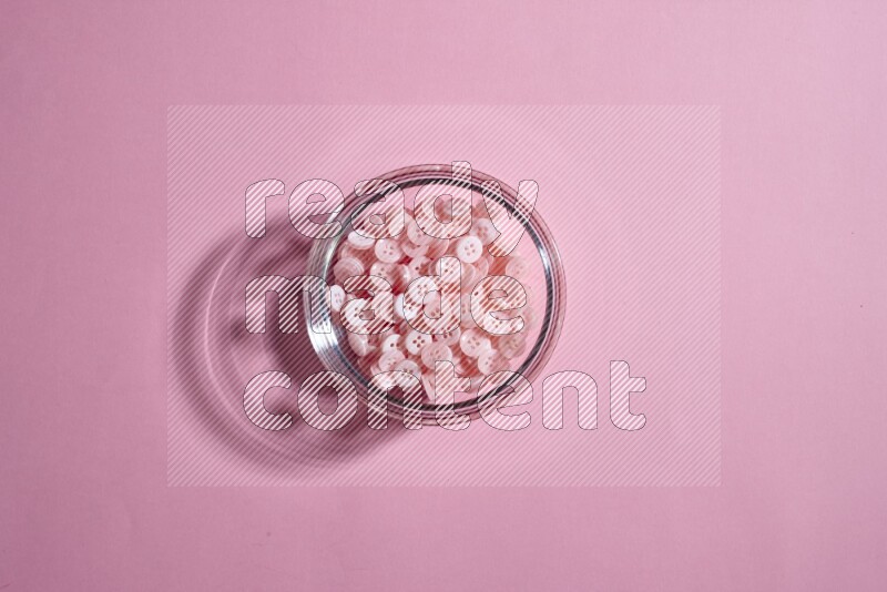 Colored buttons in a glass bowl on rose background