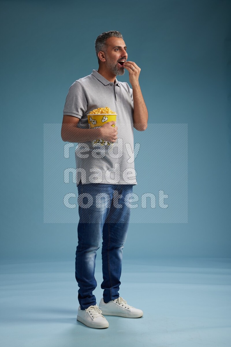 Man Standing eating popcorn on blue background