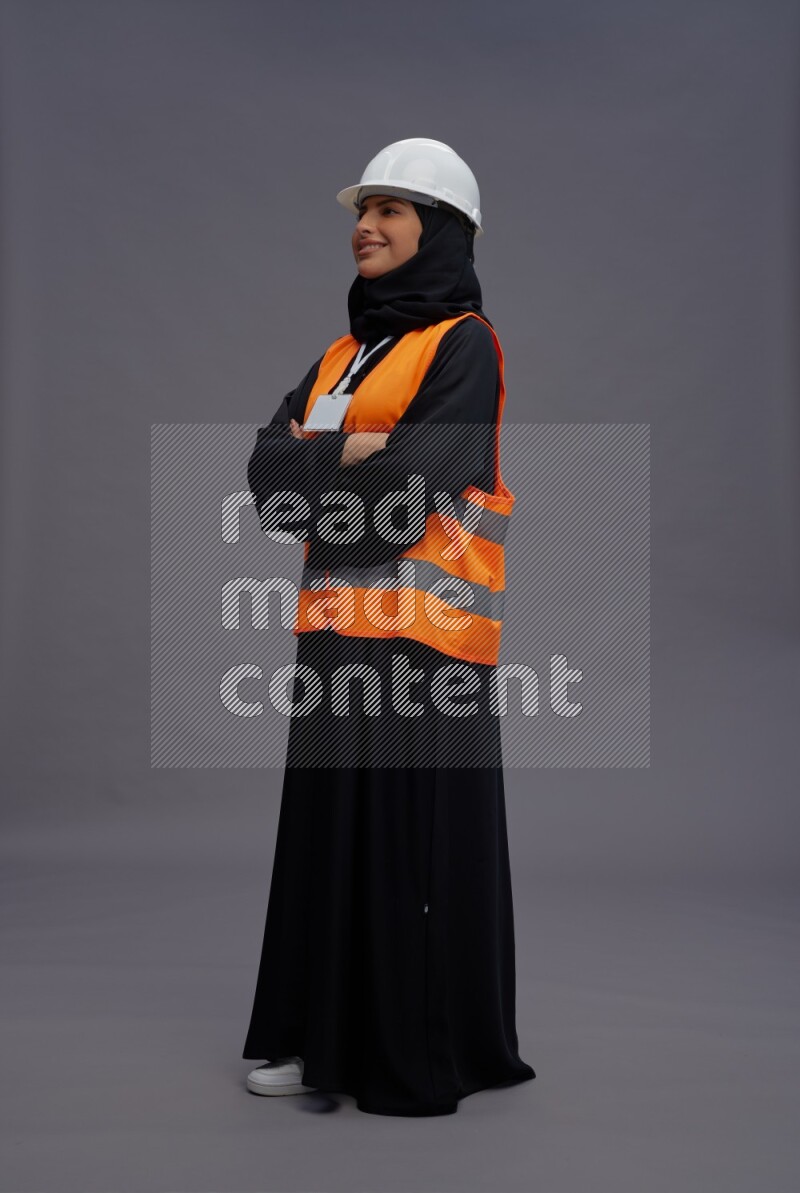Saudi woman wearing Abaya with engineer vest with neck strap employee badge standing with crossed arms on gray background