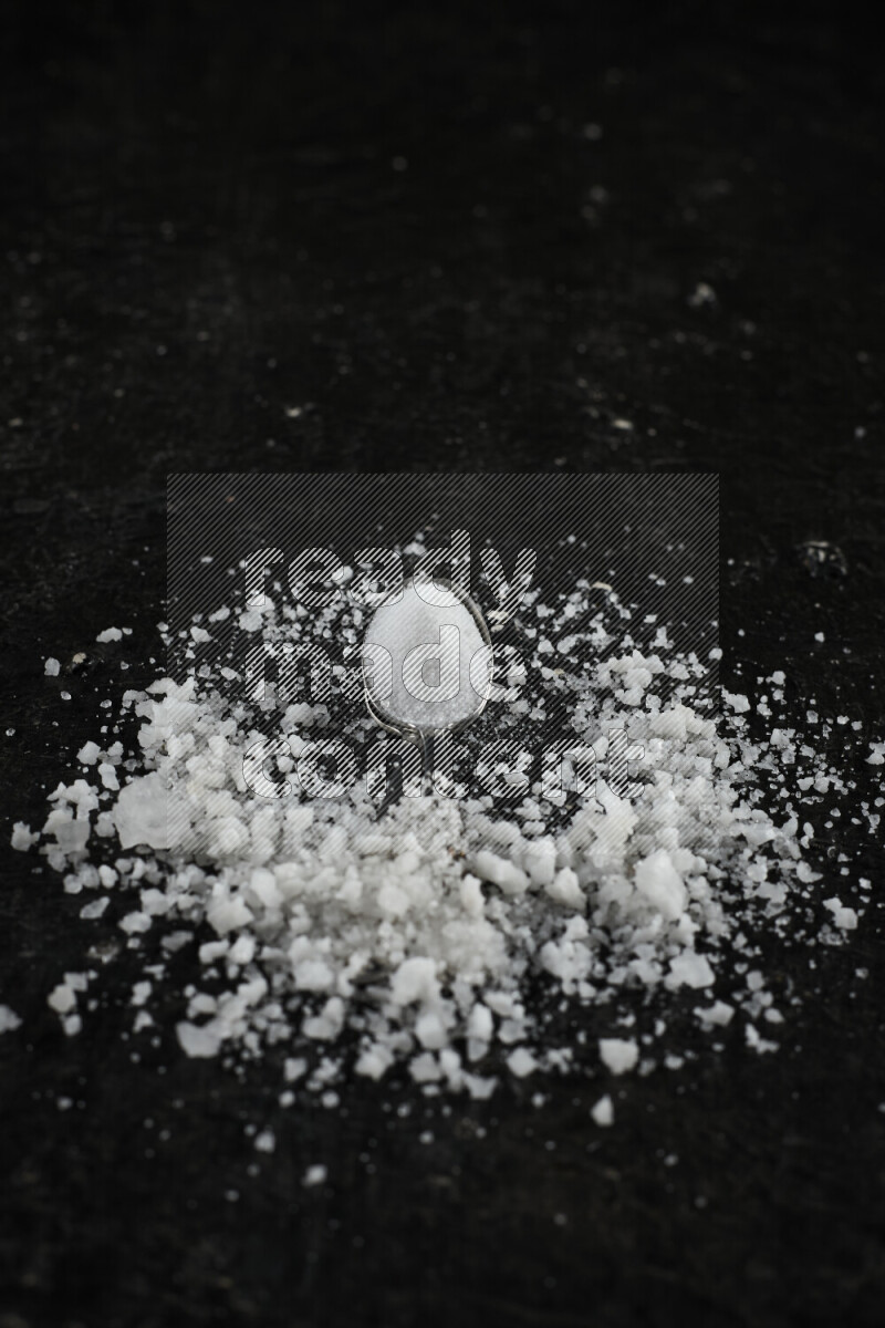2 metal spoons filled with white salt on black background