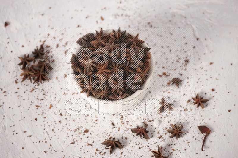 Star Anise in a white bowl and more of it sprinkled on white background