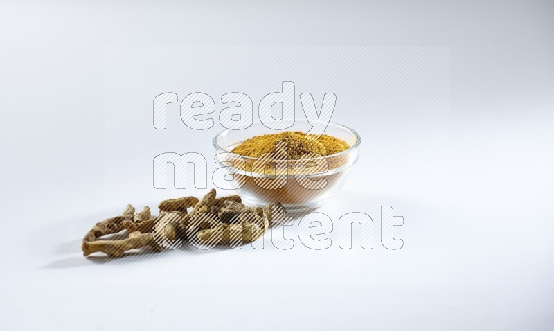 وعاء زجاجي ممتلئ ببودرة الكركم وأصابع الكركم المجففة تحته على خلفية بيضاء