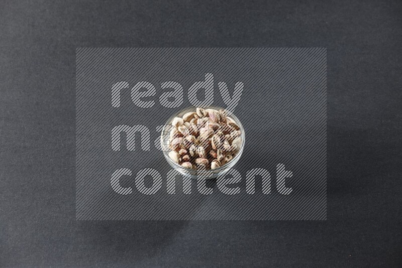 A glass bowl full of peeled pistachios on a black background in different angles
