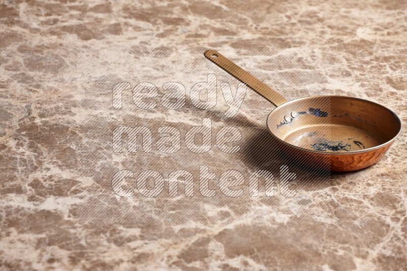 A small copper pan on beige marble background