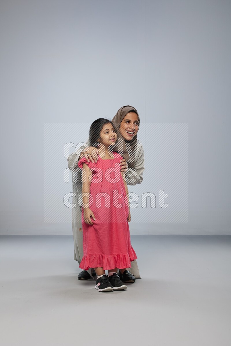 A girl and her mother interacting with the camera on gray background