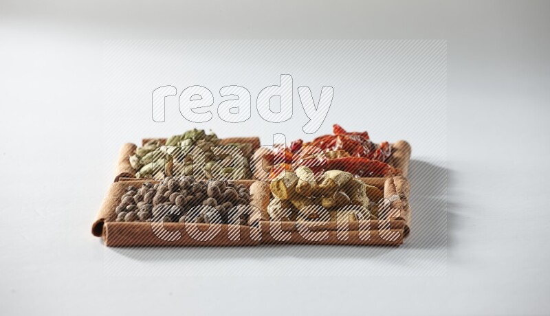 4 مربعات من أعواد القرفة ممتلئة بالفلفل الأحمر المجفف والهيل وأصابع الكركم وبهار الفلفل الحلو على أرضية بيضاء