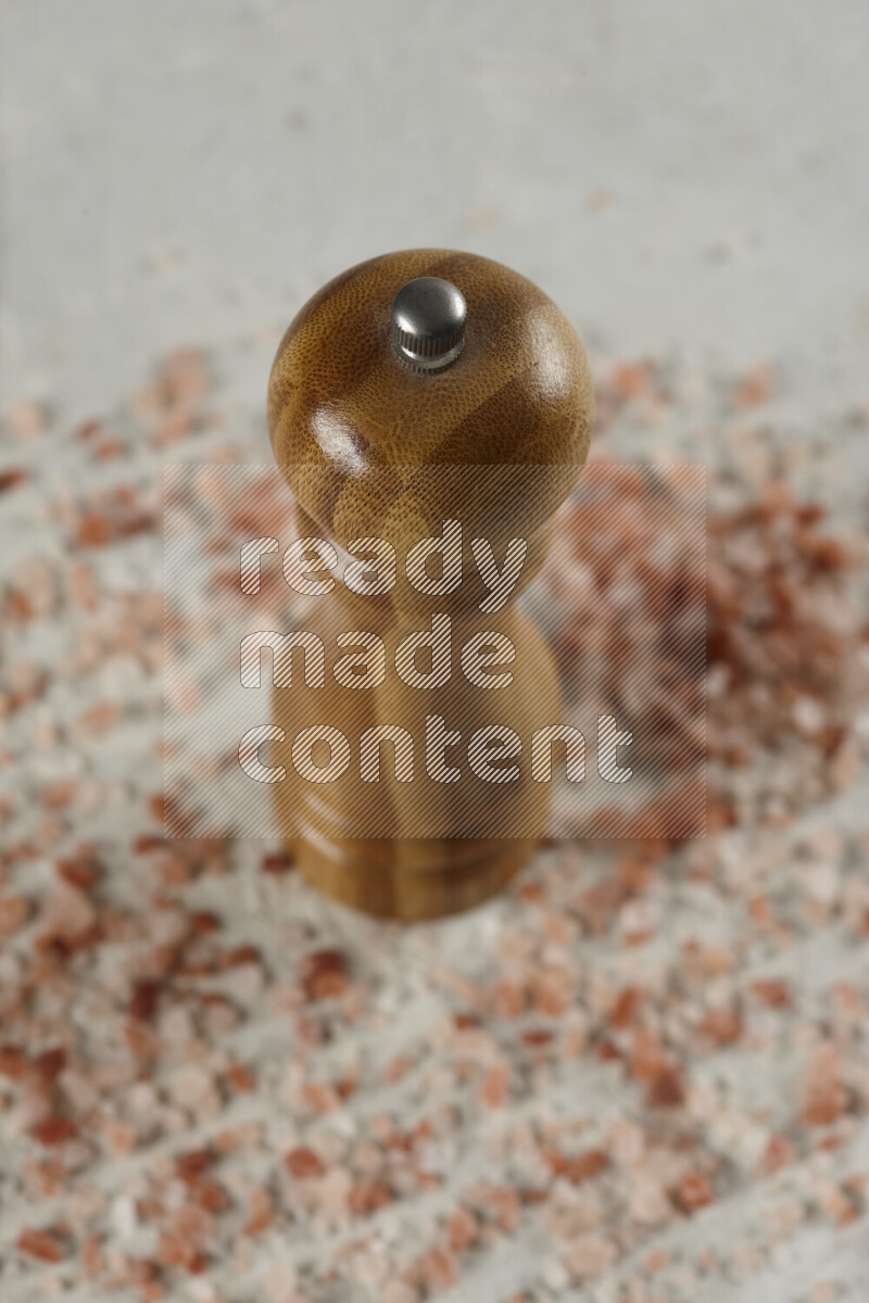 A wooden grinder standing upright and surrounded by coarse pink himalayan salt on white background