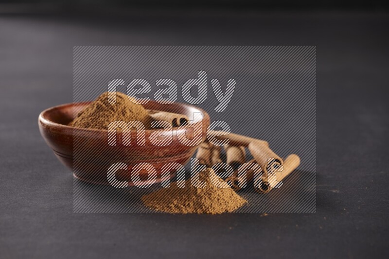 Cinnamon powder in a wooden bowl with a cinnamon sticks on black background