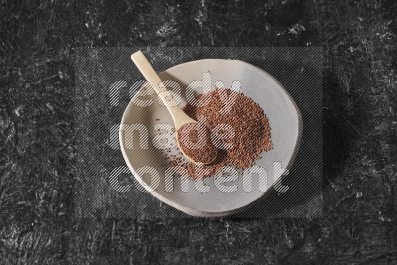 A multicolored pottery plate full of garden cress seeds and wooden spoon full of seeds on a textured black flooring