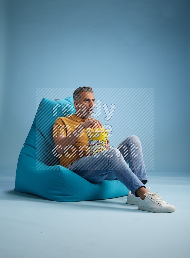 A man sitting on a blue beanbag and eating popcorn