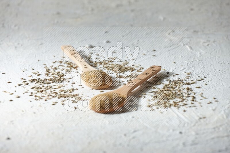 2 Wooden spoons full of cumin powder and cumin seeds on textured white flooring