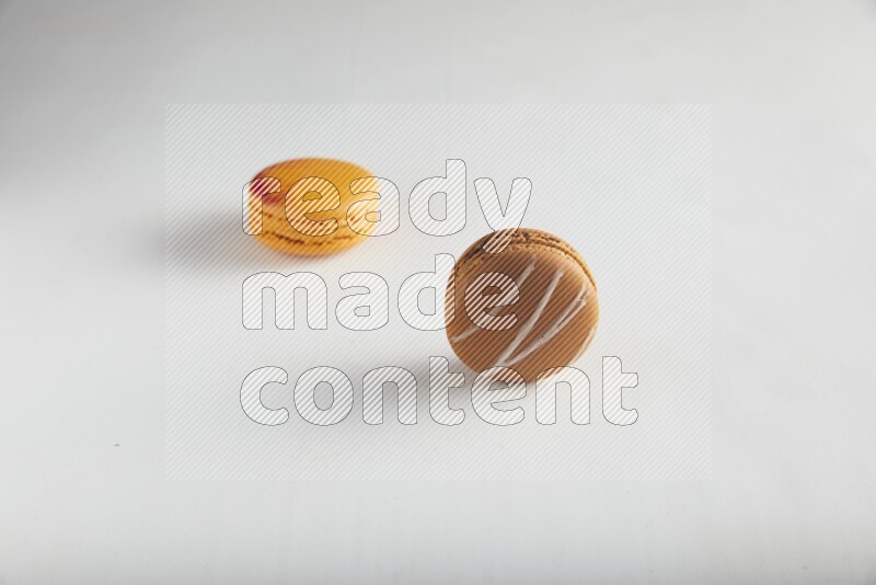 45º Shot of of two assorted Brown Irish Cream, and Orange Exotic macarons on white background