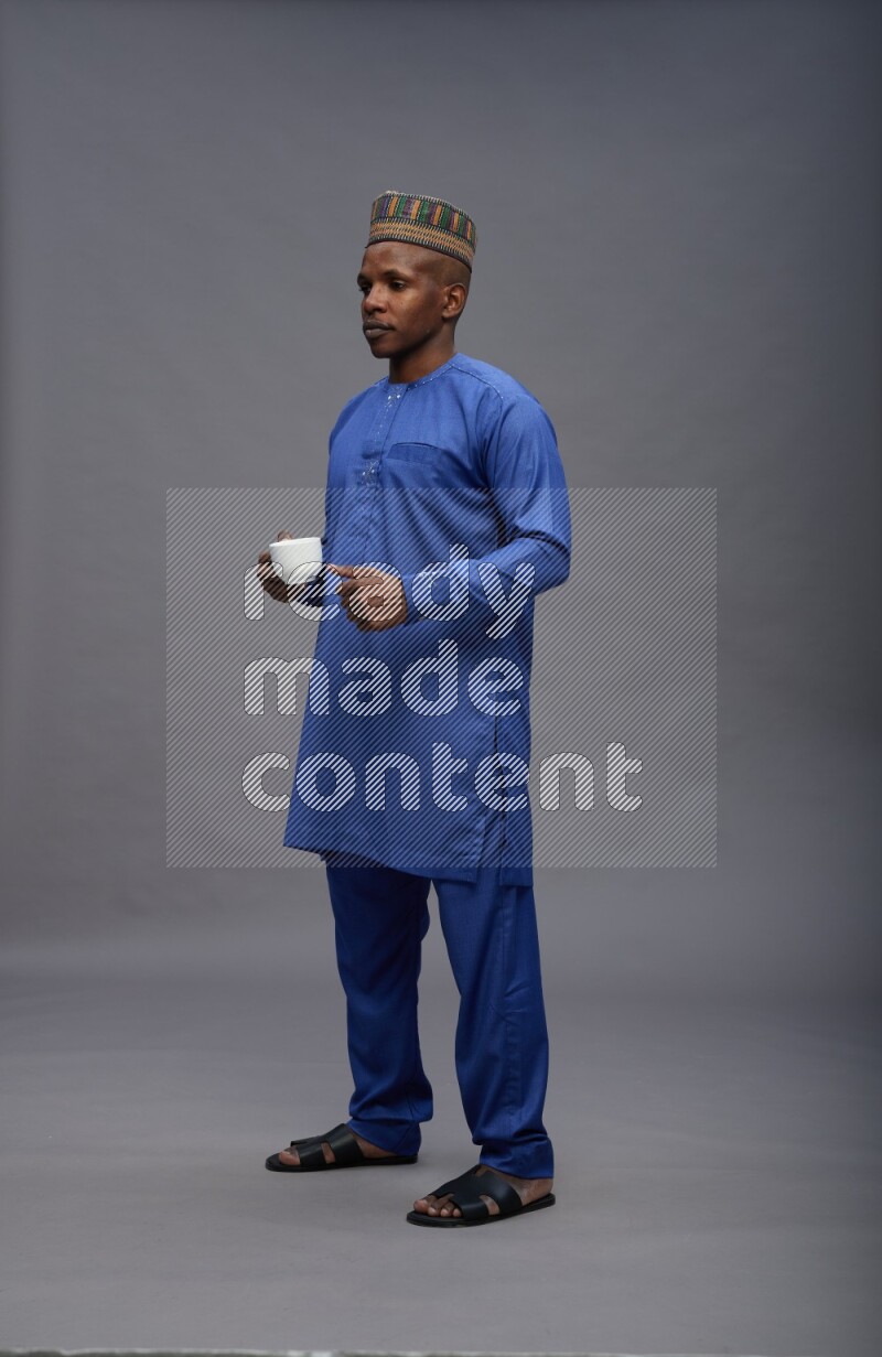 Man wearing Nigerian outfit standing holding mug on gray background