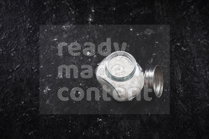 وعاء زجاجي ممتلئ بملح البحر الخشن على خلفية سوداء