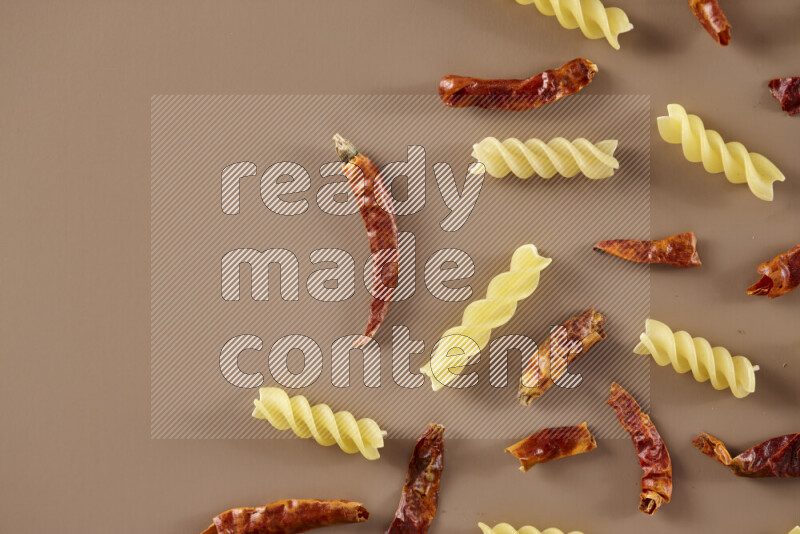 Raw pasta with different ingredients such as cherry tomatoes, garlic, onions, red chilis, black pepper, white pepper, bay laurel leaves, rosemary and cardamom on beige background