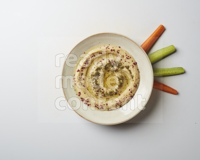 Hummus in a pottry plate garnished with zaatr & sumak on a white background